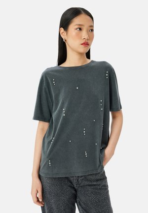 T-shirt corto grigio scuro a maniche corte con una vestibilità ampia, una texture morbida e borchie decorative sparse sulla parte anteriore.