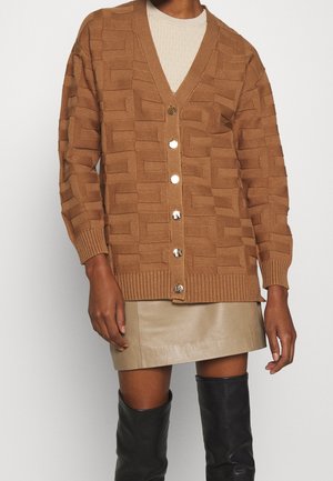 Bruine gebreide cardigan met een V-hals, met grote knopen en een geribde zoom. Gemaakt over een licht sweater en een leren rok.