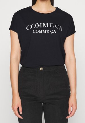 Sort kortærmet t-shirt med hvid tekst "COMME CI COMME ÇA" i et buet design. Kombineret med sorte fløjlsbukser.
