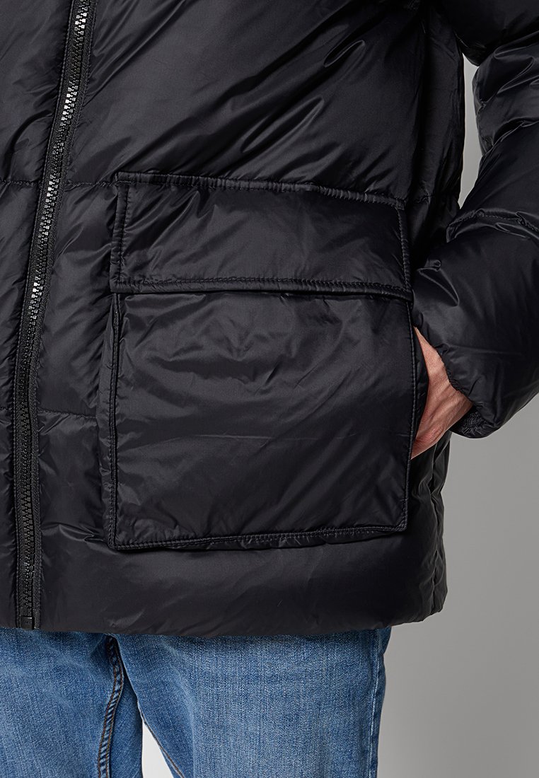 Schwarze Steppjacke mit glänzendem Finish, ausgestattet mit einem Frontreißverschluss, einer großen aufgesetzten Tasche und elastischen Bündchen für zusätzlichen Wärme.