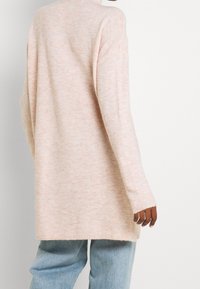 Langärmliger, hellrosa Pullover mit einer weichen Textur, lockerer Passform und seitlichen Schlitzen. Kombiniert mit locker sitzenden, hellblauen Jeans.