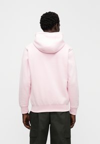 Bluza z kapturem w jasnoróżowym kolorze, wykonana z miękkiego materiału. Posiada duży kaptur, ściągacze na mankietach i w pasie. Połączona z ciemnozielonymi bojówkami.