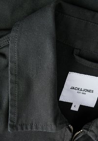 Col de chemise en tissu noir avec une étiquette blanche visible indiquant "JACK & JONES EST. 1990" et la taille "L" à l'intérieur de l'encolure.