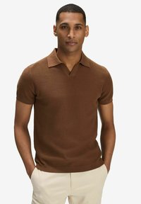 Brun randig kortärmad polo med V-hals och veckad krage. Slät textur, figurnära passform, kombinerad med ljusfärgade byxor.