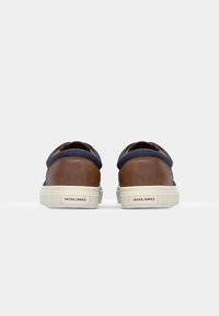 Leather and fabric casual shoes in brown and navy, featuring a rounded toe, cream outsole, and logo on the heel. Flat slip-on design.
