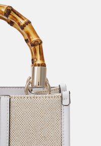 Borsa con un corpo in tessuto beige texturizzato, dettagli in pelle bianca e una maniglia in bambù. Presenta accessori metallici e un design strutturato.