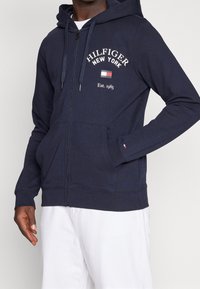 Sudadera con capucha y cremallera en tejido suave, con texto blanco "Hilfiger New York", bolsillo delantero y capucha con cordón. Puños y bajo acanalados.
