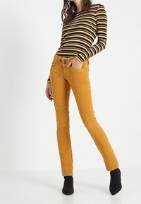 Hořčicové kordové kalhoty s pětipocket designem, dvěma předními knoflíky a slim fit. V páru s černobílým pruhovaným dlouhým rukávem.