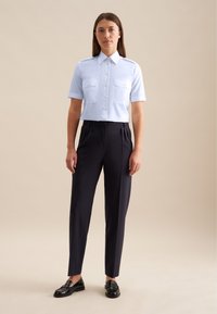 Camicia azzurra a maniche corte con colletto e due tasche sul petto, abbinata a pantaloni scuri neri tagliati su misura e mocassini neri. Texture lisce.