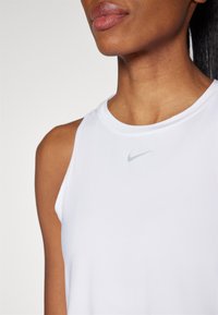 Top atletico bianco senza maniche in tessuto leggero e liscio. Presenta un piccolo logo Nike grigio nella zona del petto.