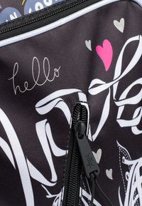 Borsa in tessuto nera con testo e design grafico bianchi, inclusi cuori e una cerniera con hardware nero. Caratterizza un motivo colorato e giocoso.