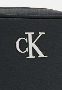 Borsa nera con texture, caratterizzata da un accento in argento con il logo "ck". Il materiale sembra essere pelle sintetica, con un design elegante.