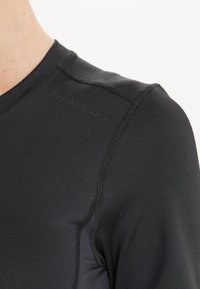 Lähikuva henkilöstä, joka wear mustaa urheilullista kompressiopaitaa, jossa on "Kestävyys" -teksti olkaommelta.