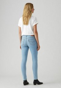 Vaaleansiniset skinny-farkut korkealla vyötäröllä, joissa on huomaamattomatommot ompelutiedot, yhdistetty valkoiseen paitaan ja mustiin nilkkureihin. Sujuva pinta.