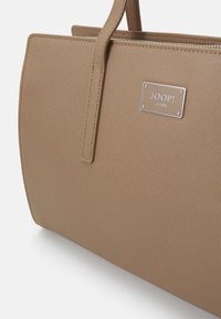 Borsa beige con materiale sintetico testurizzato, forma rettangolare, due manici robusti e una placca con logo argento sul davanti.