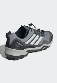Scarpa grigia da esterno con parte superiore testurizzata, caratterizzata da una suola nera, strisce bianche e un sistema di chiusura sicura con lacci integrati.