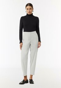 Zwarte coltrui, lichtgewicht met lange mouwen, gecombineerd met lichtgrijze maatwerkbroek. Glanzende zwarte loafers maken de look af.