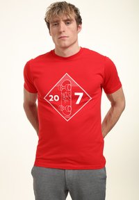Rød bomulds t-shirt med en hvid diaman grafik, hvor der står tallene "20" og "7" samt en skateboard-illustration i midten. Rund hals.