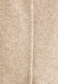Tela de fieltro beige con una textura suave, que presenta una costura central que corre de forma vertical. La superficie muestra variaciones sutiles en el color.