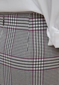 Pantalon en mélange de laine présentant un motif pied-de-poule noir et blanc avec des accents violets, fermeture éclair et coupe ajustée.