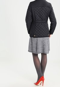 Black quilted jacket with a fitted waist, paired with a gray skirt. Features red high heels and sheer tights, emphasizing the layered outfit.