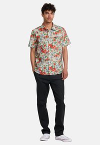 Short-sleeve floral shirt featuring a multicolored pattern of red, orange, and purple flowers on a light background, paired with black pants.