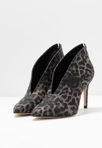 Botines con estampado de leopardo, punta afilada y tacón alto de aguja. Fabricados con tela texturizada en negro y beige, con un diseño en forma de V.