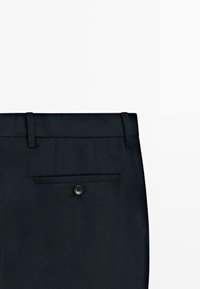 Zwarte broek met een vlakke voorkant, riemlussen en een enkele achterzak met een sluiting met twee knopen. Glad, geweven stoftextuur.