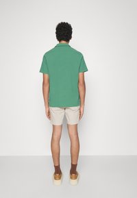 Grön kortärmad skjorta i bomull, ihopparad med beiga shorts. Bruna ankelsockor och ljusbruna plattformssneakers kompletterar outfiten.