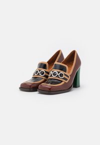 Talons hauts en cuir verni marron et noir avec des bordures beiges, des talons bloc verts et des embellissements en chaîne argentée sur le devant.