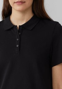 Polo noir avec un col plat, une patte de boutonnage à trois boutons et des manches courtes. Fabriqué en tissu texturé pour le confort.