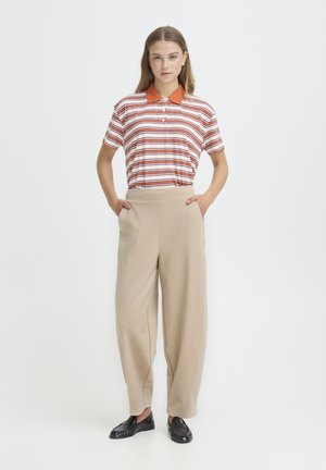 Striped polo shirt with orange collar, beige wide-leg trousers, and black loafers. Model stands with hands in pockets against a white background.