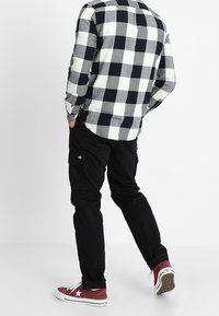 Camisa de cuadros en blanco y negro con un dobladillo redondeado, combinada con pantalones cargo negros y zapatillas rojas con acentos blancos.