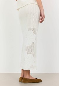 Fustă midi albă din tricot, cu un model perforat și decupaje florale la tiv, asortată cu pantofi flat din suede maro, prezentată dintr-un unghi lateral.