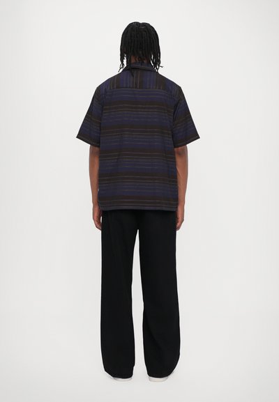 Chemise à manches courtes avec col, rayée bleu foncé et noir, assortie à un pantalon noir ample et des chaussures blanches. Texture lisse, coupe décontractée.