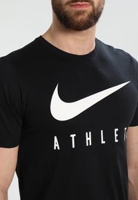 Hombre que lleva una camiseta negra con el swoosh blanco de Nike y la palabra parcial "ATHLET" visible en el frente.
