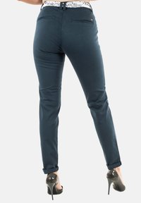 Donkerblauwe strakke broek met een gladde textuur, voorzien van achterzakken en een opgerolde zoom. Gepaard met glanzende zwarte hoge hakken.