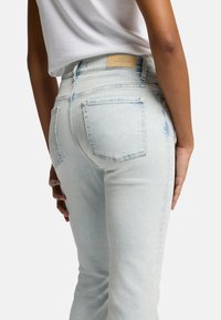 Jeans in denim blu chiaro con una forma aderente, dotati di due tasche posteriori e un'etichetta tessuta in vita. Finitura strutturata e pulita.
