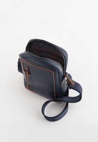 Námořnická kožená crossbody taška se zipovým uzávěrem, akcenty oranžového prošití, nastavitelným popruhem a texturovanou vnitřní podšívkou.