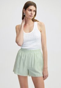 Débardeur blanc à petits pois noirs, associé à un short vert clair mi-long en tissu texturé avec une taille élastique.