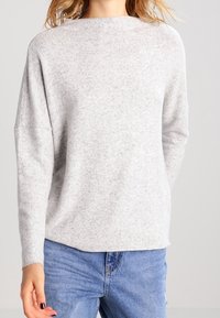 Ljusgrå tröja gjord av mjukt tyg, med rund halsringning, sänkta axlar och en avslappnad passform. Kombinerad med blå denimjeans.