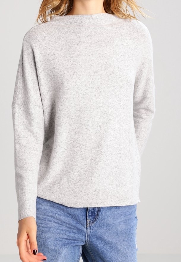 Ljusgrå tröja gjord av mjukt tyg, med rund halsringning, sänkta axlar och en avslappnad passform. Kombinerad med blå denimjeans.