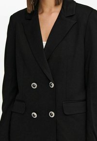 Černý dvouřadý blazer vyrobený z hladké tkaniny, se stříbrně akcentovanými knoflíky a dvěma předními kapsami. Strukturovaný design klopy.