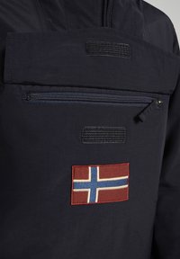 Giacca navy con una tasca zip prominente, caratterizzata da un dettaglio ricamato della bandiera norvegese rossa e blu e una finitura in tessuto testurizzato.