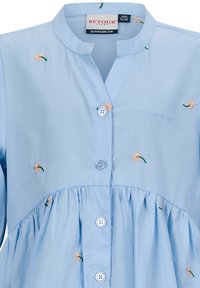 Hellblaues Hemd mit Kragen, das mit gestickten Blumen und grünen Akzenten verziert ist, mit einer Knopfleiste und einem gerafften Taillendetail. Weicher Stoff.