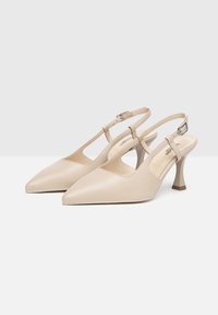Tacchi slingback in pelle beige con punta affusolata, sottili cinturini alla caviglia e tacco medio scolpito. Texture liscia, minimalismo nei dettagli.