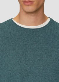 Pull en teinte sarcelle texturé avec un col rond. Le col intérieur présente un accent blanc, créant un effet superposé. Tissu lisse et doux.