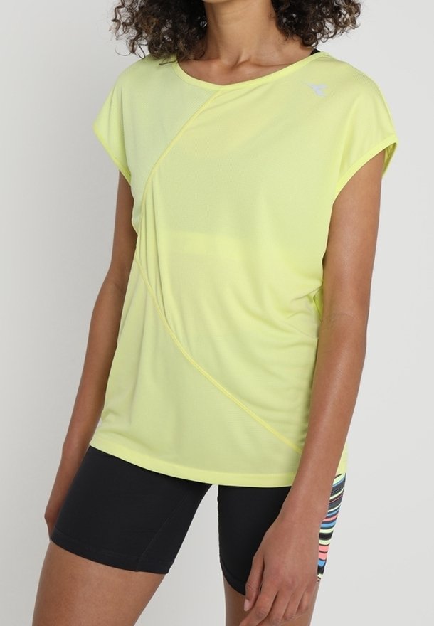 Top deportivo de manga corta de color amarillo brillante con detalles de costura en diagonal, combinado con pantalones cortos negros con rayas horizontales multicolores.