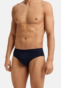Donkerblauwe slip gemaakt van zachte, rekbare stof met een tailleband met reliëfbranding. Ontworpen met een strakke pasvorm en minimale naden.