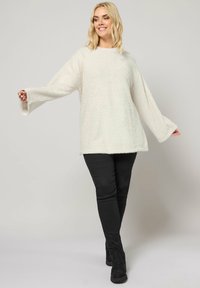 Un pull oversize blanc et duveteux avec des manches larges, un tissu texturé et un col rond, assorti à un pantalon noir slim.